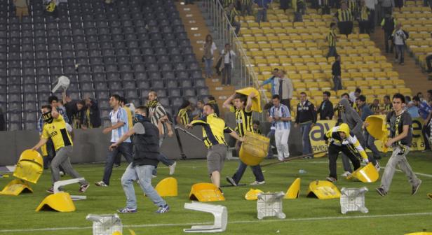 Fußballfans randalieren in einem Stadion und werfen mit Sitzen um sich.
