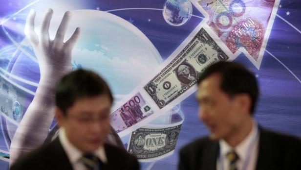 Eine stilisierte Darstellung von Dollar, Euro und Yuan vor einem Globus, mit zwei Personen im Vordergrund.