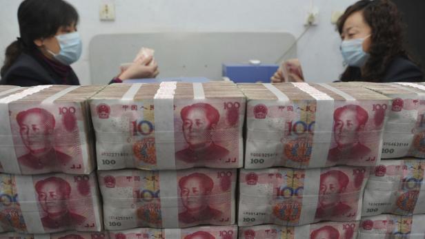 Zwei Frauen mit Gesichtsmasken zählen Bündel chinesischer Yuan-Banknoten.