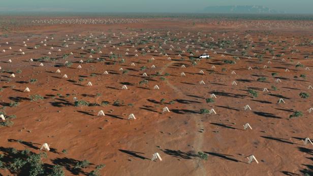Eine weite, rote Landschaft mit vielen kleinen Zelten und einem weißen Geländewagen.