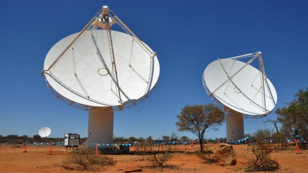 Zwei große Radioteleskope stehen in einer trockenen, roten Landschaft unter blauem Himmel.