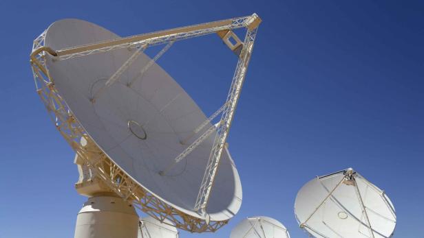 Mehrere weiße Radioteleskope stehen unter einem blauen Himmel.