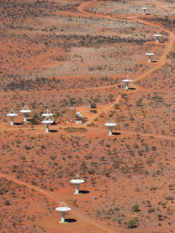 Luftaufnahme einer Reihe von Radioteleskopen in einer trockenen, roten Landschaft.