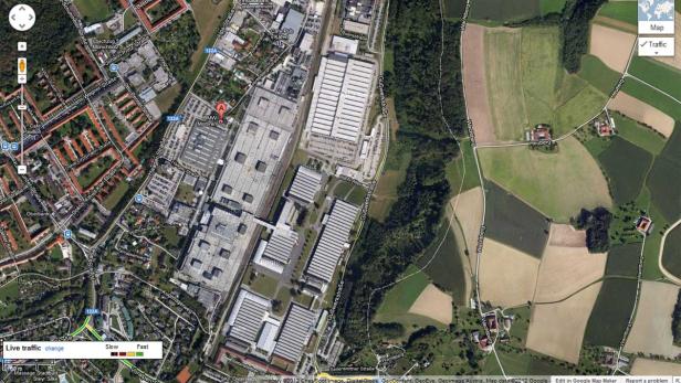 Eine Luftaufnahme des BMW-Werks in Steyr, Österreich, umgeben von Feldern und Wohngebieten.