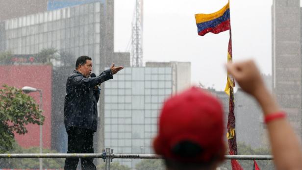 Hugo Chávez spricht während eines Regenschauers vor einer venezolanischen Flagge.