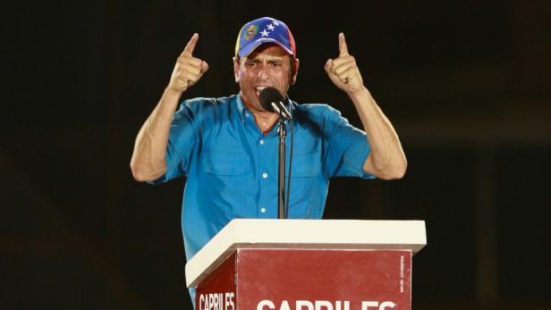 Ein Mann mit einer Kappe mit venezolanischer Flagge gestikuliert an einem Rednerpult.