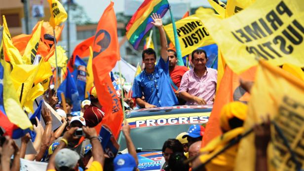 Zwei Männer stehen auf einem Auto, umgeben von Anhängern mit Flaggen bei einer Kundgebung.