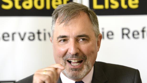 Ein Mann mit Bart lächelt vor einem Banner der „Stadler Liste“.