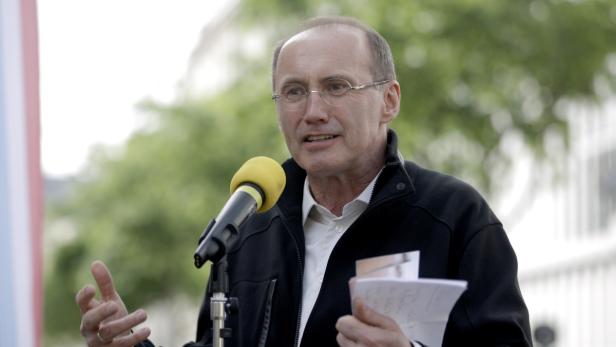 Ein Mann mit Brille spricht in ein gelbes Mikrofon und hält Notizen in der Hand.