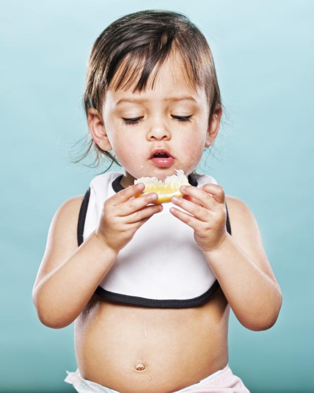 Ein kleines Mädchen mit Lätzchen isst eine Zitronenscheibe und verzieht das Gesicht.