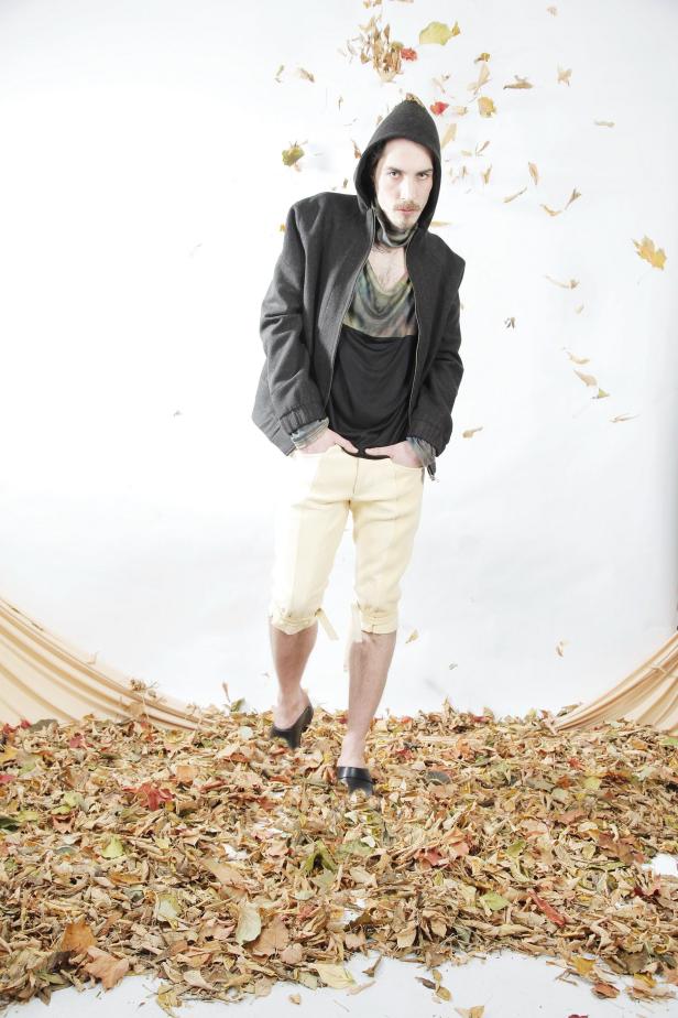 Ein Mann mit Kapuzenjacke steht in einem Haufen Herbstlaub, während Blätter von oben fallen.