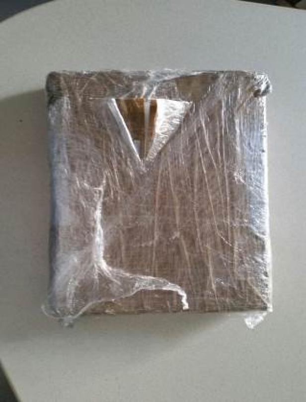 Ein in Klarsichtfolie verpacktes, quadratisches Paket liegt auf einem Tisch.