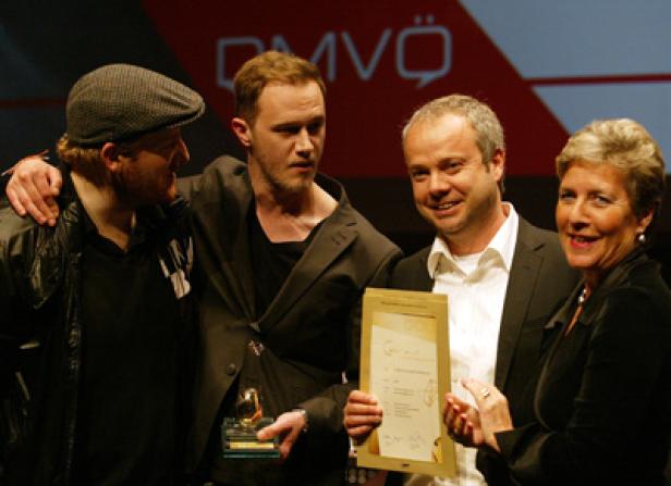 Vier Personen posieren mit einer Urkunde und einer goldenen Trophäe.