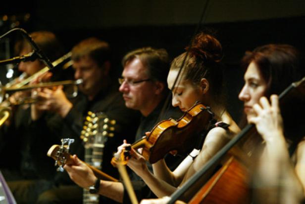 Ein Orchester spielt mit verschiedenen Instrumenten, darunter Geigen, Gitarre und Trompete.
