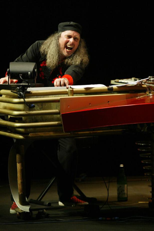 Ein Mann mit langen Haaren spielt auf einem ungewöhnlichen, metallenen Tasteninstrument und singt.