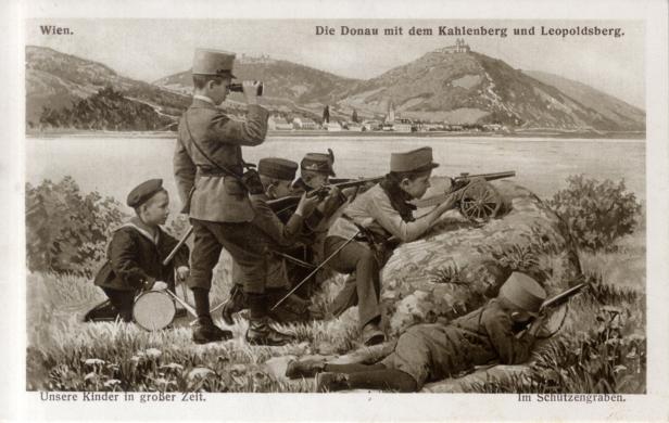 Eine Gruppe von Kindern spielt Krieg am Ufer der Donau mit Blick auf den Kahlenberg und Leopoldsberg.