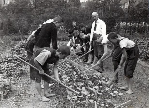 Eine Gruppe von Jungen arbeitet barfuß mit einem Mann in einem Gemüsegarten.