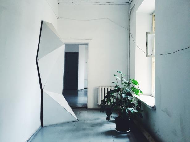 Ein Innenraum mit einer Zimmerpflanze am Fenster und einer geometrischen Skulptur.