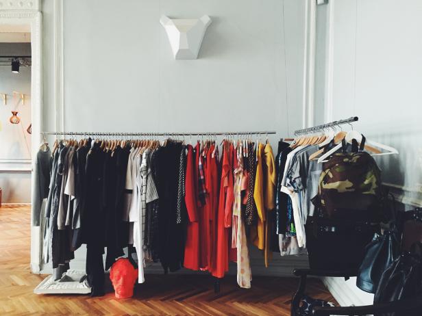 Zwei Kleiderständer mit bunter Kleidung in einem hellen Raum mit Fischgrätenparkett.