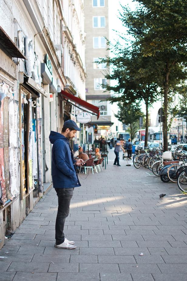 Ein Mann steht auf dem Bürgersteig und schaut auf sein Handy.