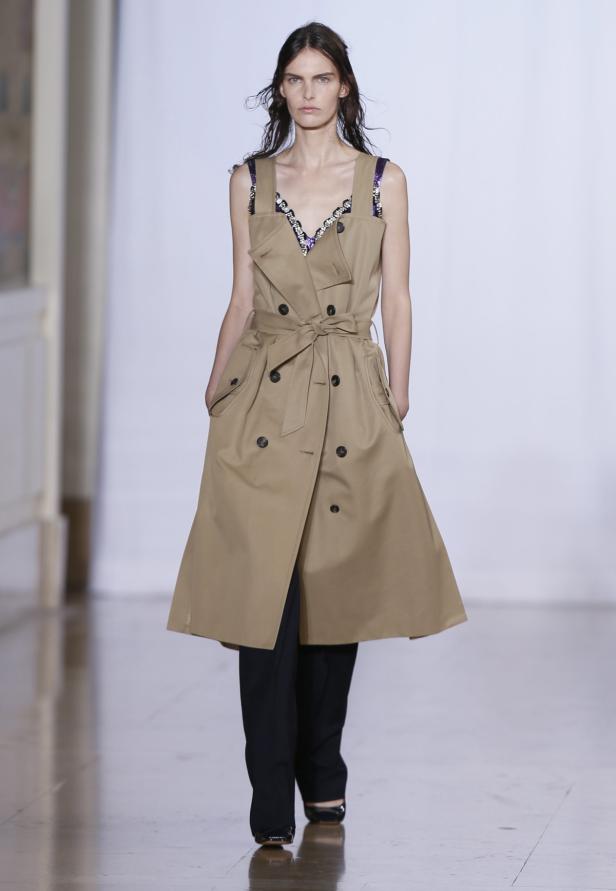 Eine Frau trägt einen beigefarbenen Trenchcoat über einer schwarzen Hose.