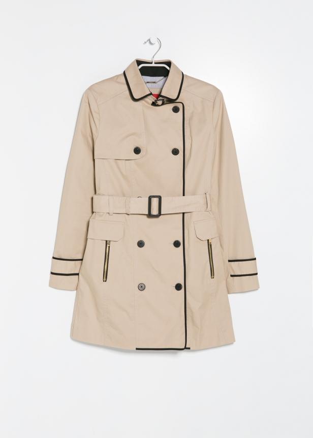 Ein beigefarbener Trenchcoat mit schwarzen Akzenten hängt an einem Kleiderbügel.