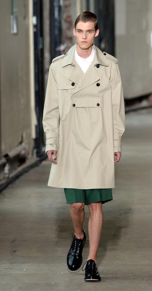 Ein Mann in einem Trenchcoat und grünen Shorts läuft auf einem Laufsteg.