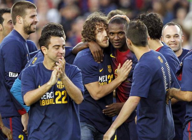 Barcelona-Spieler umarmen Éric Abidal, der ein T-Shirt mit der Aufschrift „Merci Abidal 22“ trägt.