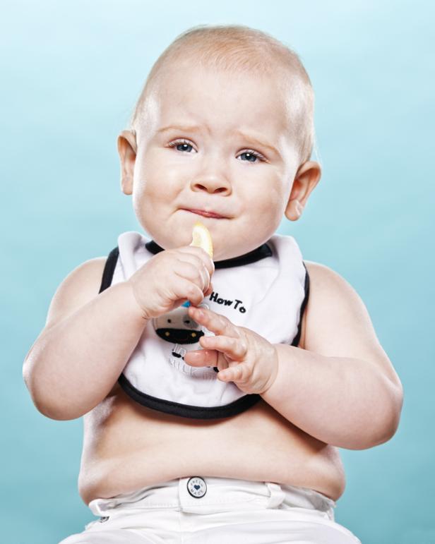 Ein Baby mit Lätzchen isst eine Zitronenscheibe und verzieht das Gesicht.