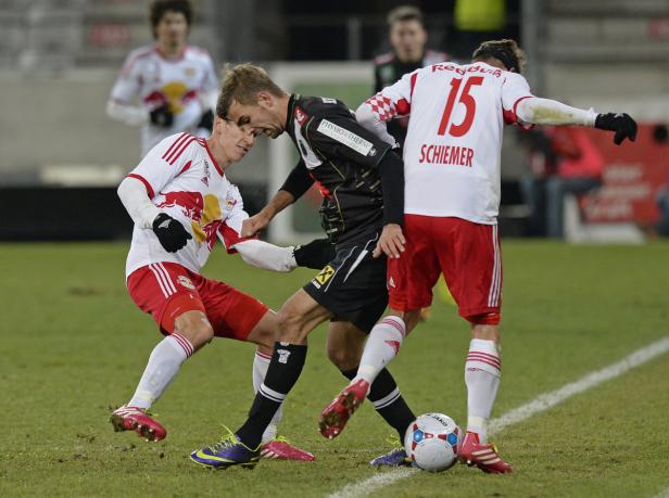 Drei Fußballspieler kämpfen um den Ball auf dem Spielfeld.