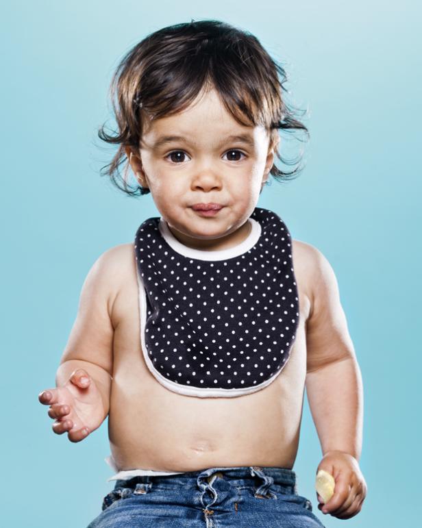 Ein Baby mit einem gepunkteten Lätzchen vor einem hellblauen Hintergrund.