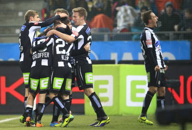 Eine Gruppe Fußballspieler in schwarz-weißen Trikots umarmt sich auf dem Spielfeld.