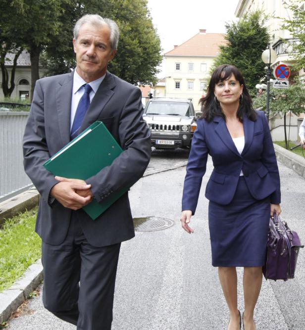Ein Mann mit Aktenordner und eine Frau mit Handtasche gehen eine Straße entlang.