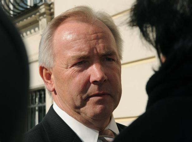 Ein Mann mit grauem Haar und Anzug steht im Gespräch mit einer anderen Person.