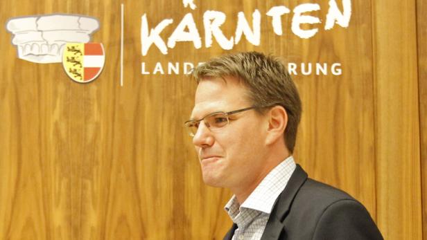 Ein Mann mit Brille steht vor einem hölzernen Hintergrund mit dem Schriftzug „Kärnten“.