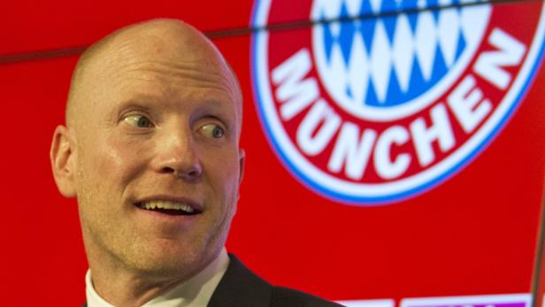 Ein Mann vor dem Logo des FC Bayern München.