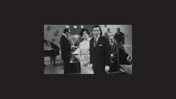 Ein Schwarzweißfoto von zwei Sängern mit Band im Hintergrund.