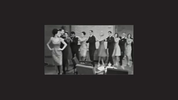 Eine Gruppe elegant gekleideter Menschen steht auf einer Bühne.