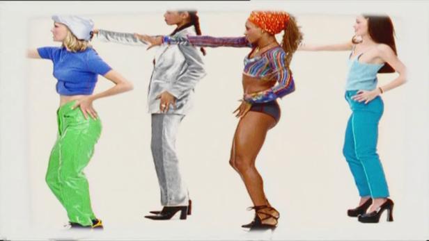 Vier Frauen in farbenfrohen Outfits posieren mit ausgestreckten Armen vor einem weißen Hintergrund.