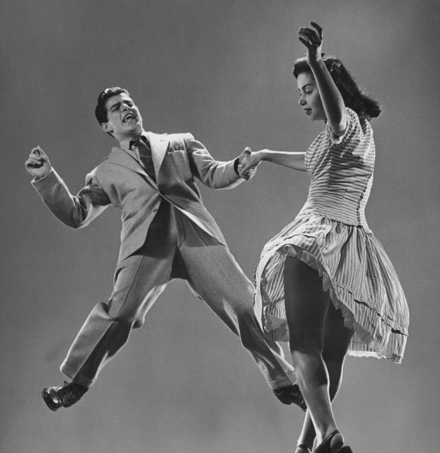 Ein Mann im Anzug und eine Frau im gestreiften Kleid tanzen ausgelassen.