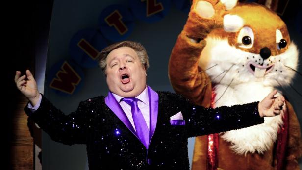 Ein Mann in einem glitzernden Sakko und ein großes Hasenkostüm stehen auf einer Bühne.