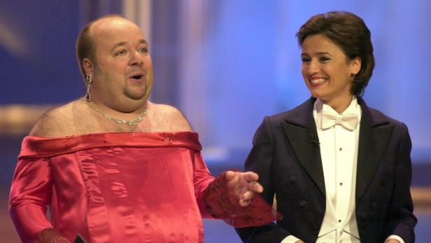 Ein Mann im roten Kleid steht neben einer lächelnden Frau im Smoking.