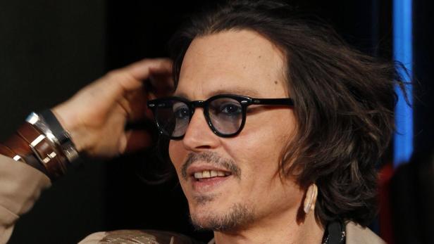 Johnny Depp mit Brille und mehreren Armbändern posiert für ein Foto.