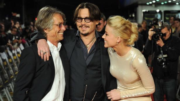 Johnny Depp posiert mit zwei weiteren Personen auf einem roten Teppich.