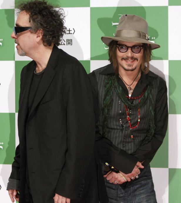 Tim Burton und Johnny Depp posieren zusammen vor einer grün-weißen Wand.
