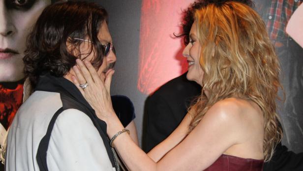 Johnny Depp und eine Frau interagieren vor einem Poster.