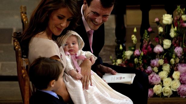 Eine Familie sitzt in einer Kirche, ein Baby in Taufkleidung auf dem Schoß der Mutter.