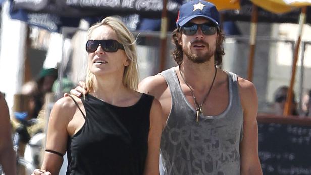 Sharon Stone mit einem Mann am Strand, beide tragen Sonnenbrillen.