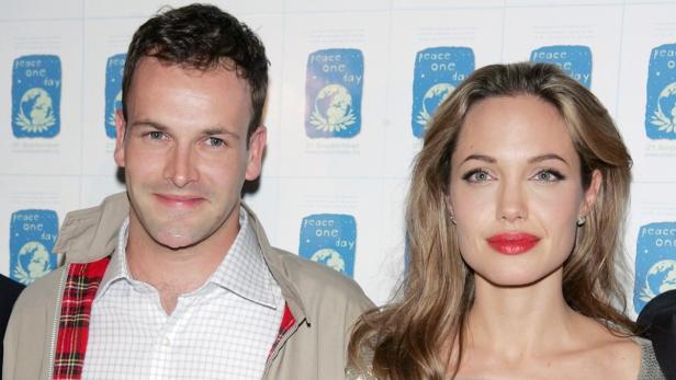 Angelina Jolie und Jeremy Gilley posieren vor einem Hintergrund mit „Peace One Day“-Logos.