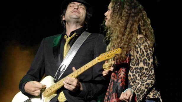 Ein Mann spielt Gitarre, während eine Frau daneben ins Mikrofon singt.